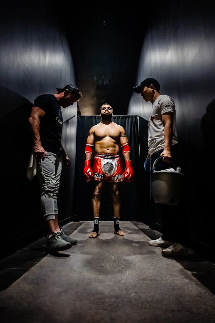 Fighter standing between two cornermen in a dark tunnel before the walkout
