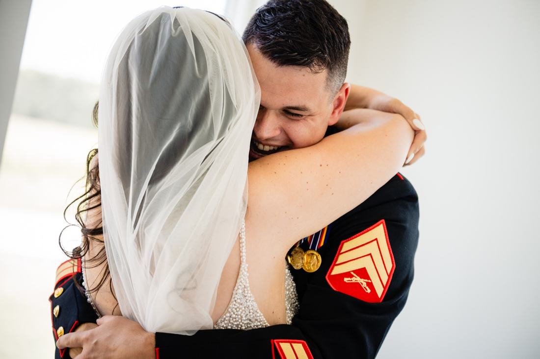 Groom in Marine dress blues laughing as his bride wraps her arms around him