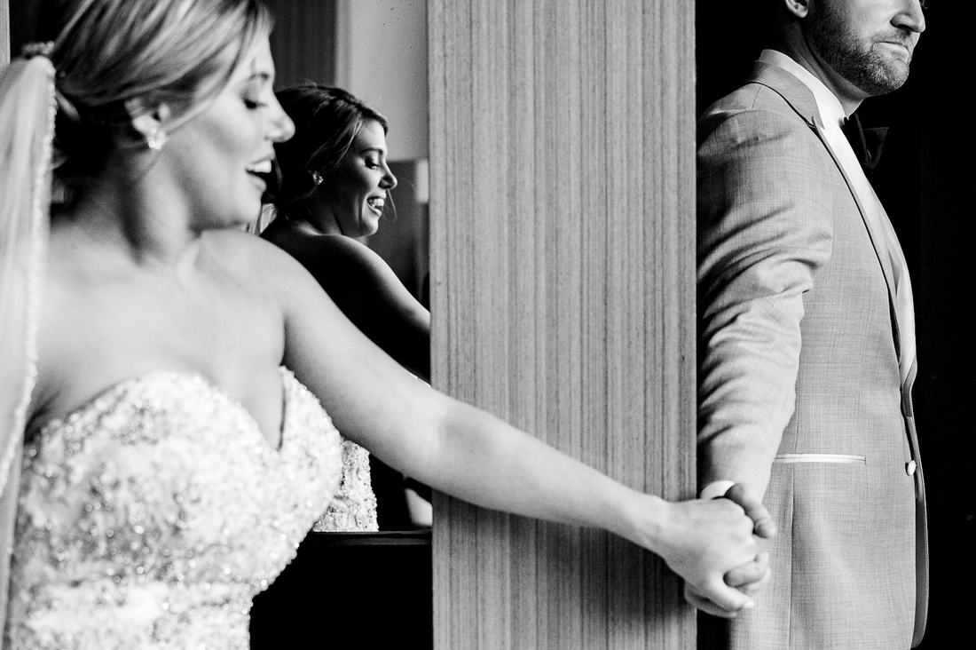Black and white first touch: bride and groom holding hands around a pillar before the ceremony
