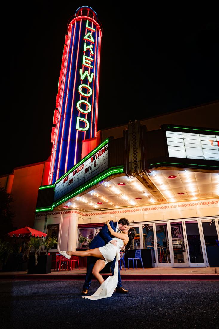 Groom dipping the bride beneath a neon theatre marquee at night